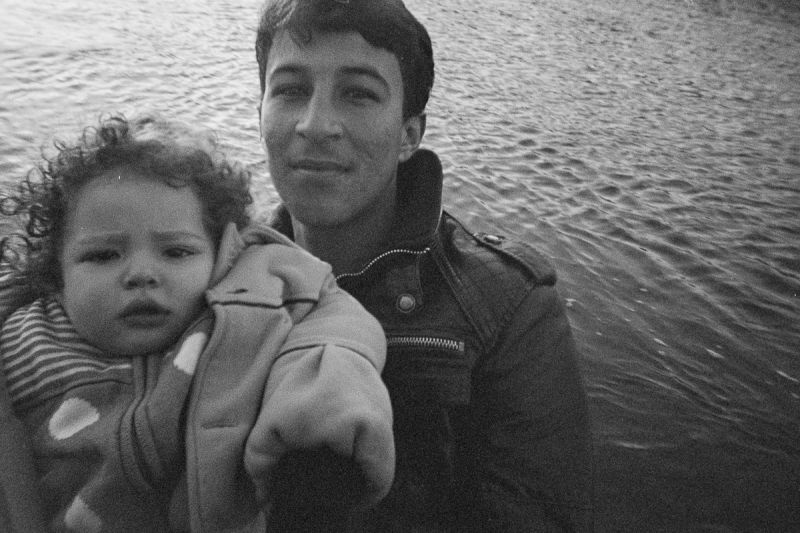 A young man looks relieved inside the camera and holds up a young girl, after they arrived in a safe harbour.