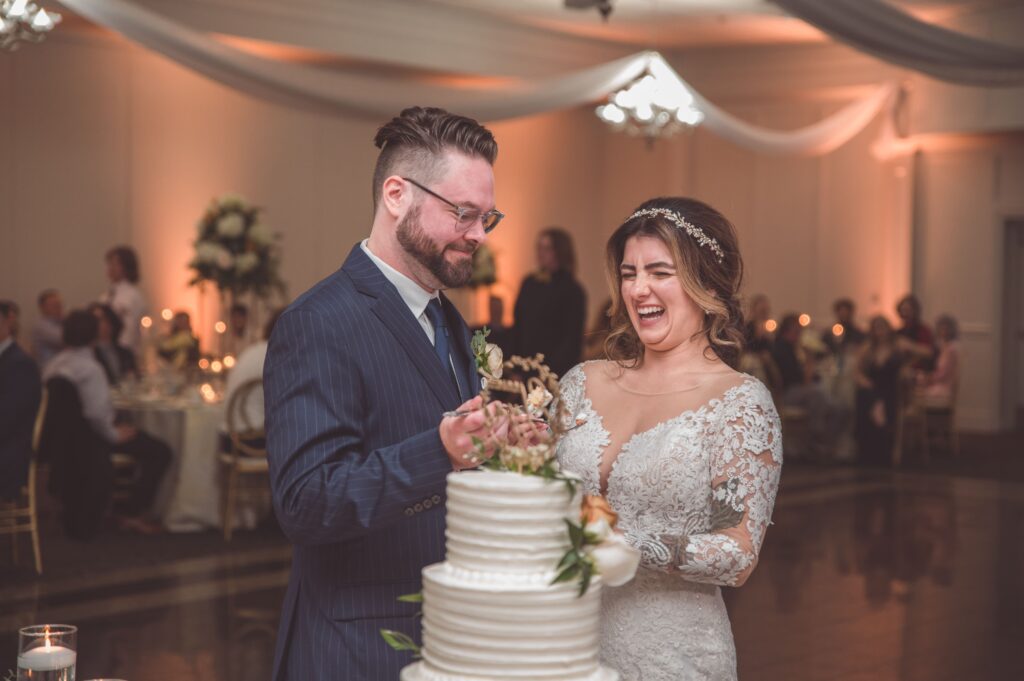 Wedding couple cutting cake with reception guests visible in background creating atmosphere and context