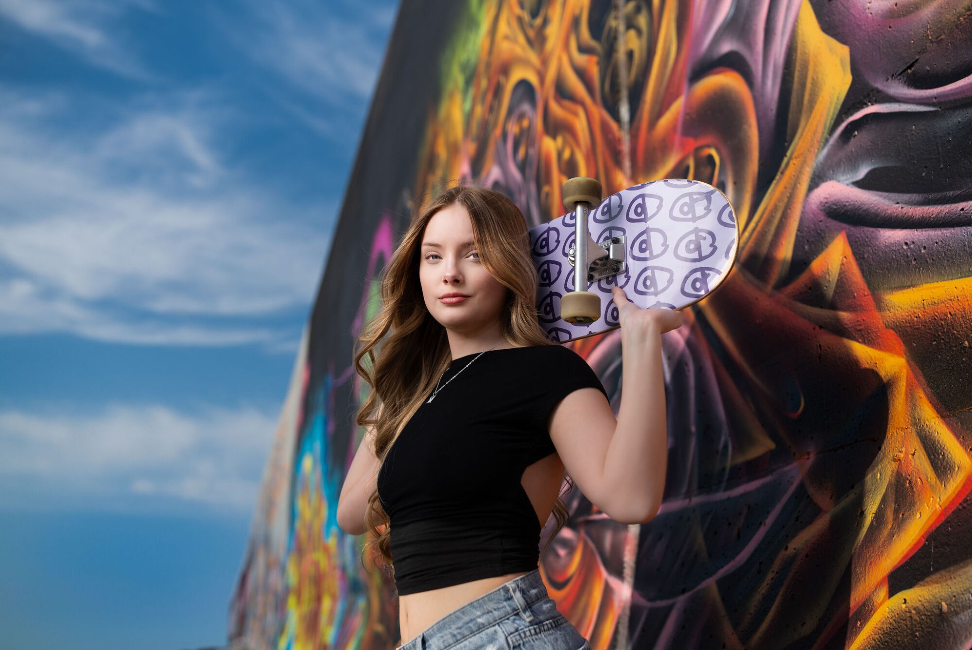 Skateboarder senior portrait with board in front of graffiti wall at urban skatepark