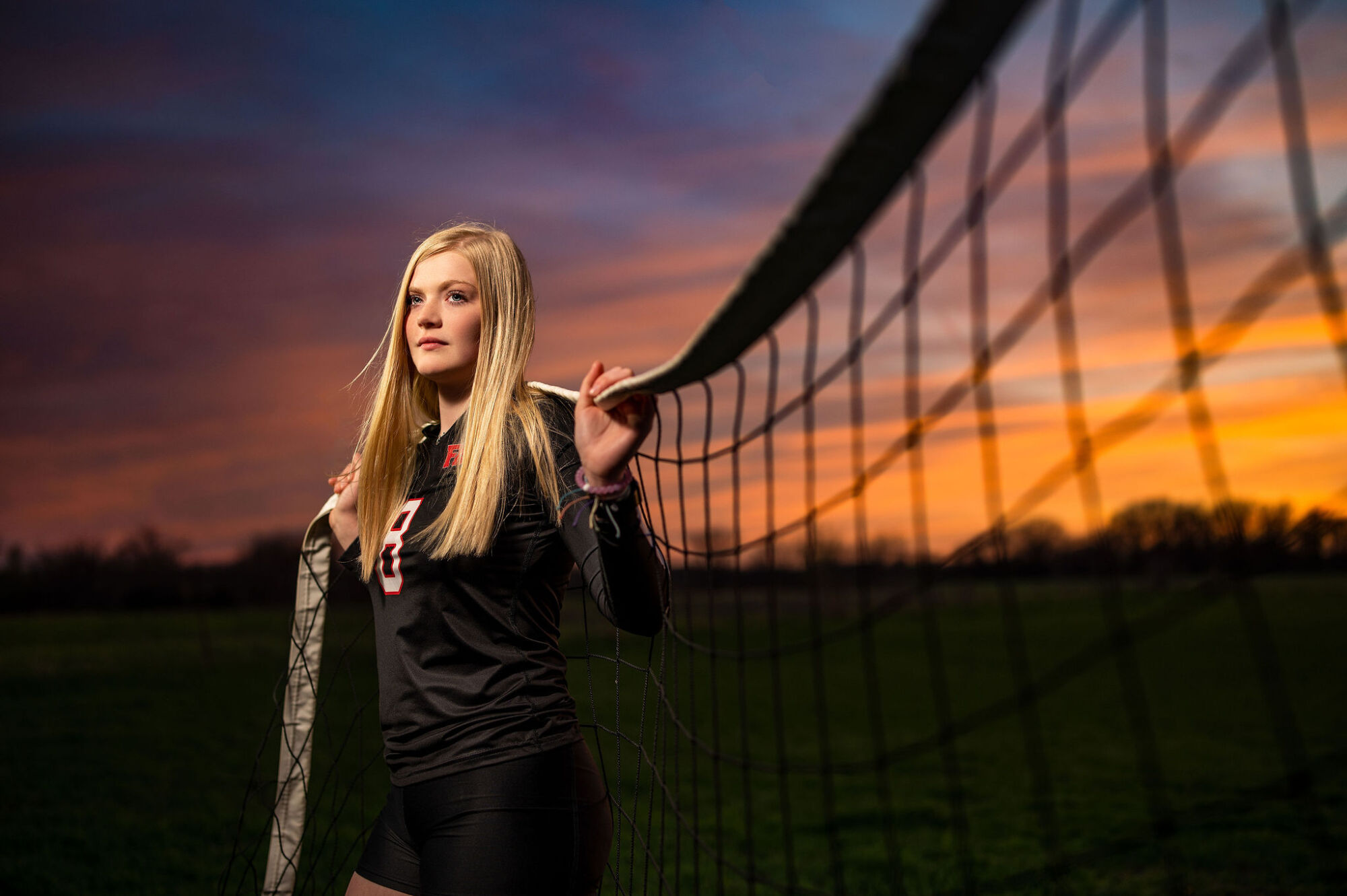 Indoor volleyball senior portrait at the net in team uniform
