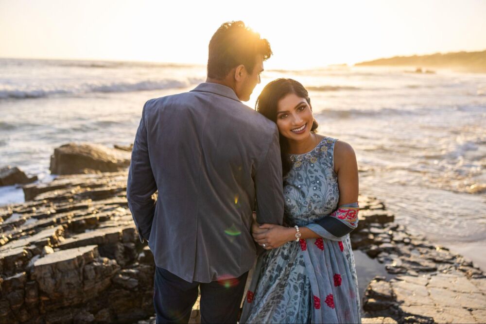 Couple stands near water at golden hour