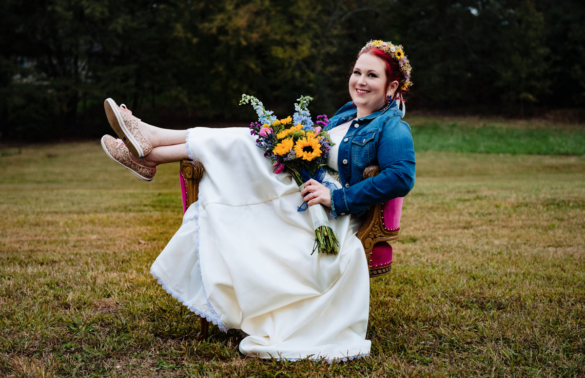 Bride for rustic boho weddings sits on a colorful chair while in a jean jacket.